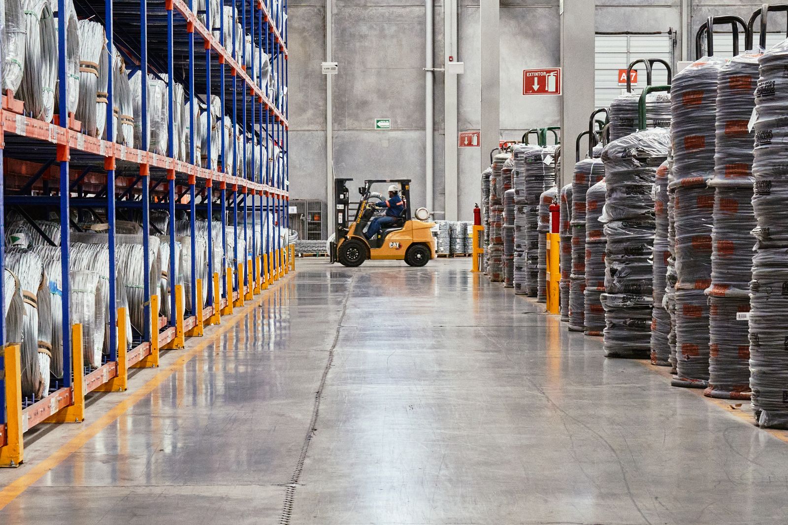 Corredor de armazém de distribuidora com empilhadeira em operação, representando a logística comercial B2B